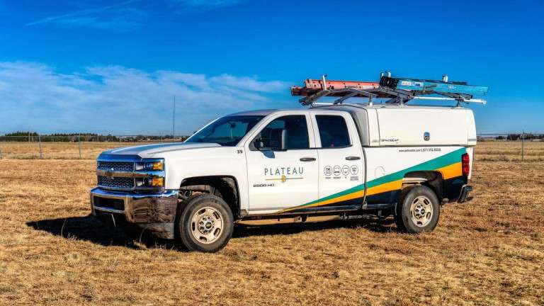 White Plateau service truck parked in a dry grass field under a blue sky with ladders on the roof