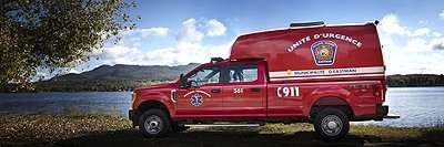SpaceKap | Home 11 Red emergency medical services vehicle parked by a lake under a blue sky with clouds