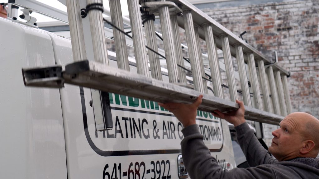 Worker lifting an aluminum ladder onto a heating and air conditioning service van