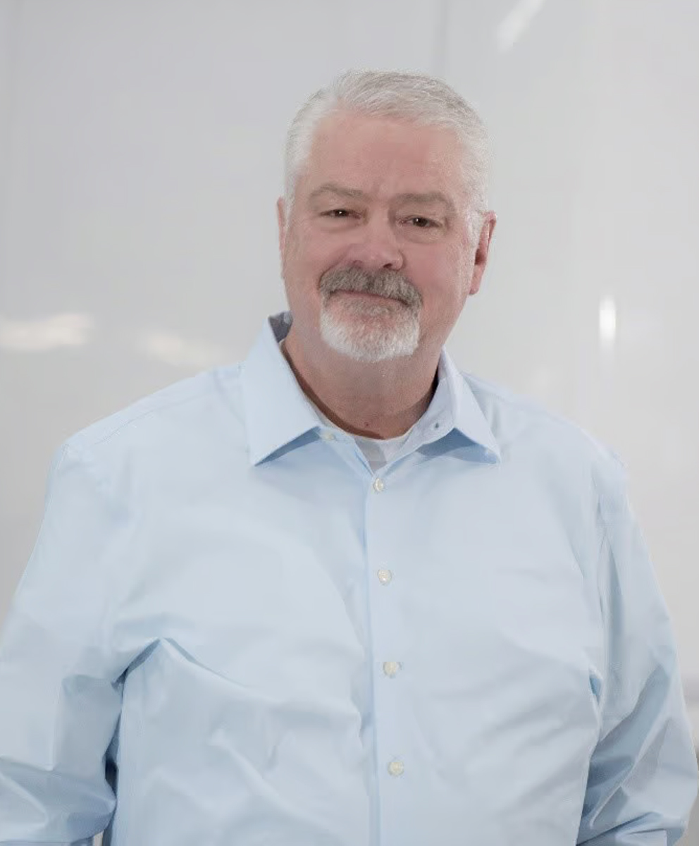 Smiling older man with white hair and beard wearing a light blue button-down shirt