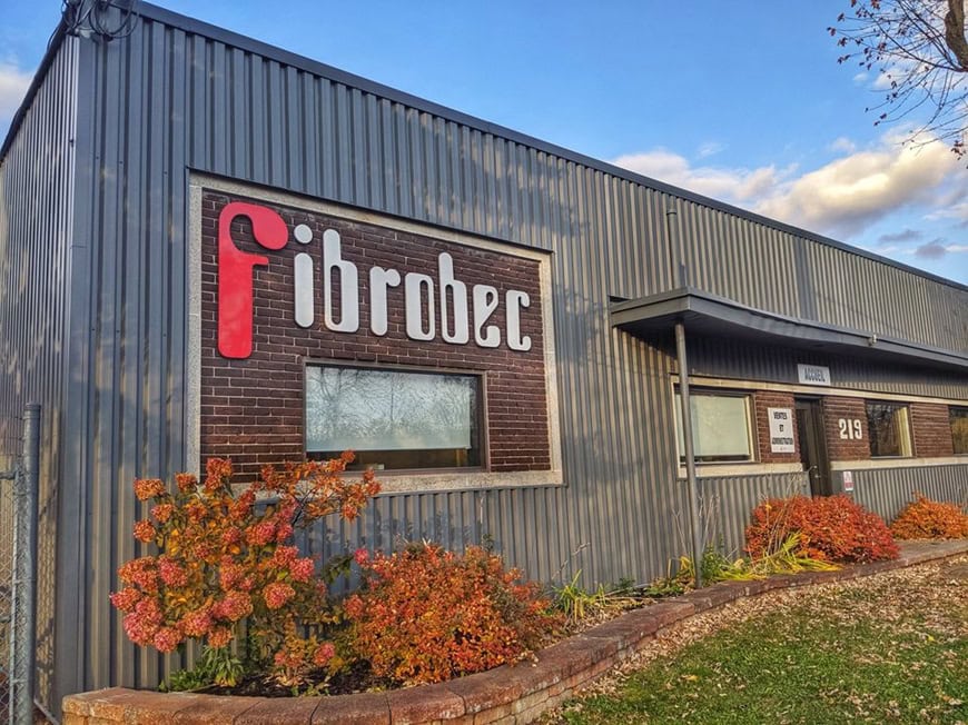 Exterior view of the Fibrobec industrial building with its logo on a brick wall panel and autumn landscaping