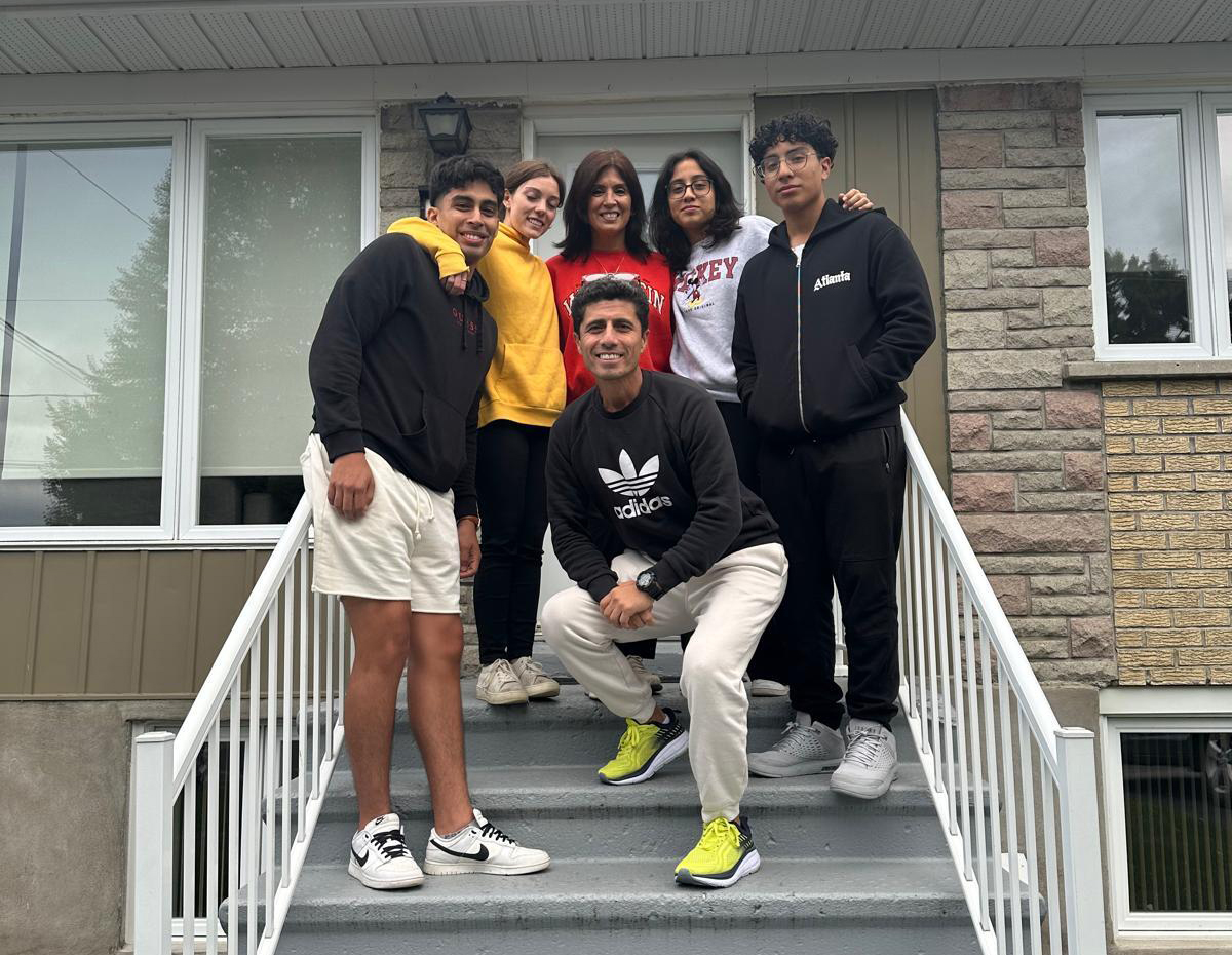 Group of six diverse young adults smiling and posing on outdoor steps in casual clothing with a house background