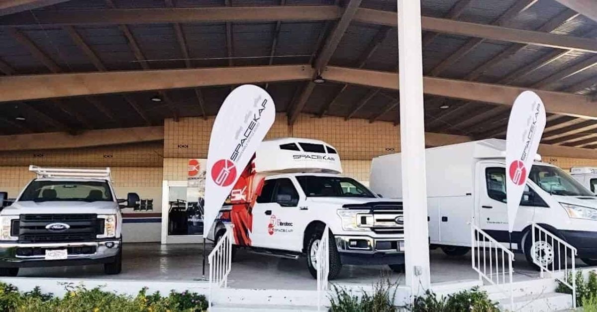 White Ford trucks displayed under a covered area with two vertical flags branded with Spacekap logos