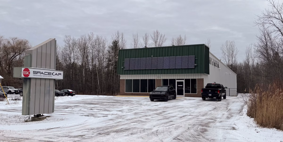 Snow-covered parking lot in front of SpaceKap commercial building with solar panels on green facade