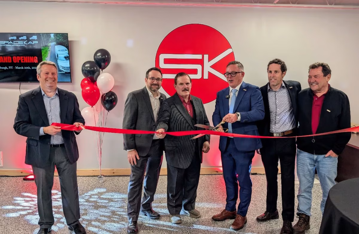 Group of six men in business attire cutting a red ribbon at the grand opening event of SPARK CAP in a decorated office space