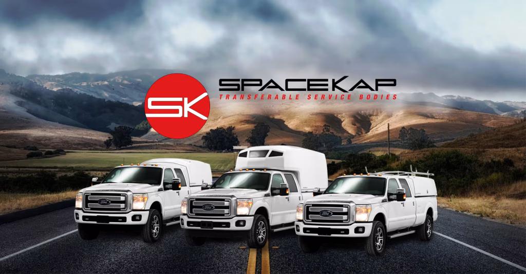 Three white Ford trucks equipped with SpaceKap transferable service bodies parked on a road with mountainous landscape and cloudy sky in background
