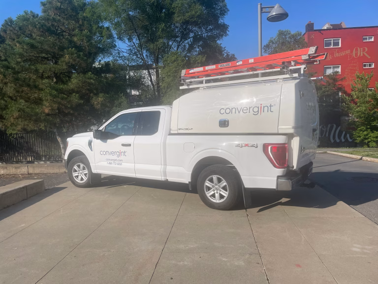 White service truck with Convergint branding parked on a concrete driveway with a red ladder on top