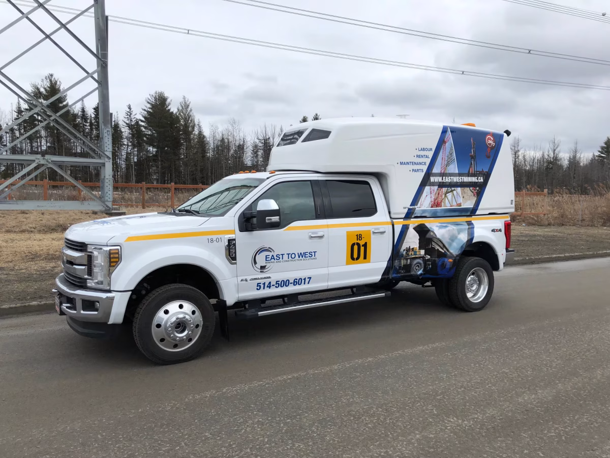 White East to West mining and construction service truck parked on a road near trees and power lines