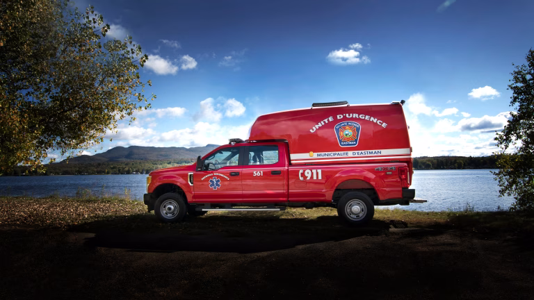 Red emergency response vehicle parked by a lake with mountains and a clear blue sky in the background