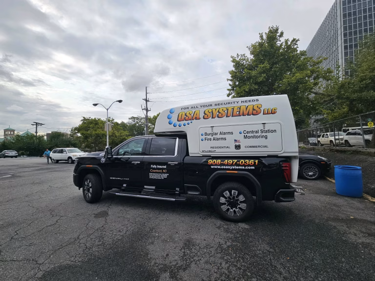 Black truck with O.S.A. Systems LLC security service advertisement parked in a lot under cloudy sky