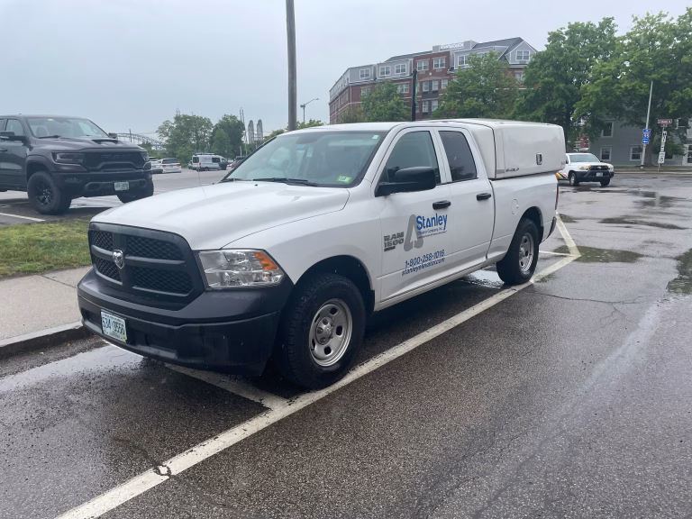White Ram 1500 pickup truck with Stanley Elevator Company Inc. logo parked on wet street