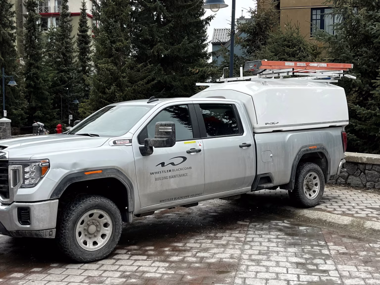 Whistler Blackcomb Building Maintenance white pickup truck parked on cobblestone near pine trees