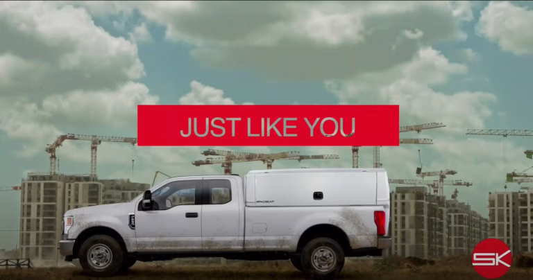 White pickup truck with canopy on construction site background and red banner reading 'JUST LIKE YOU'