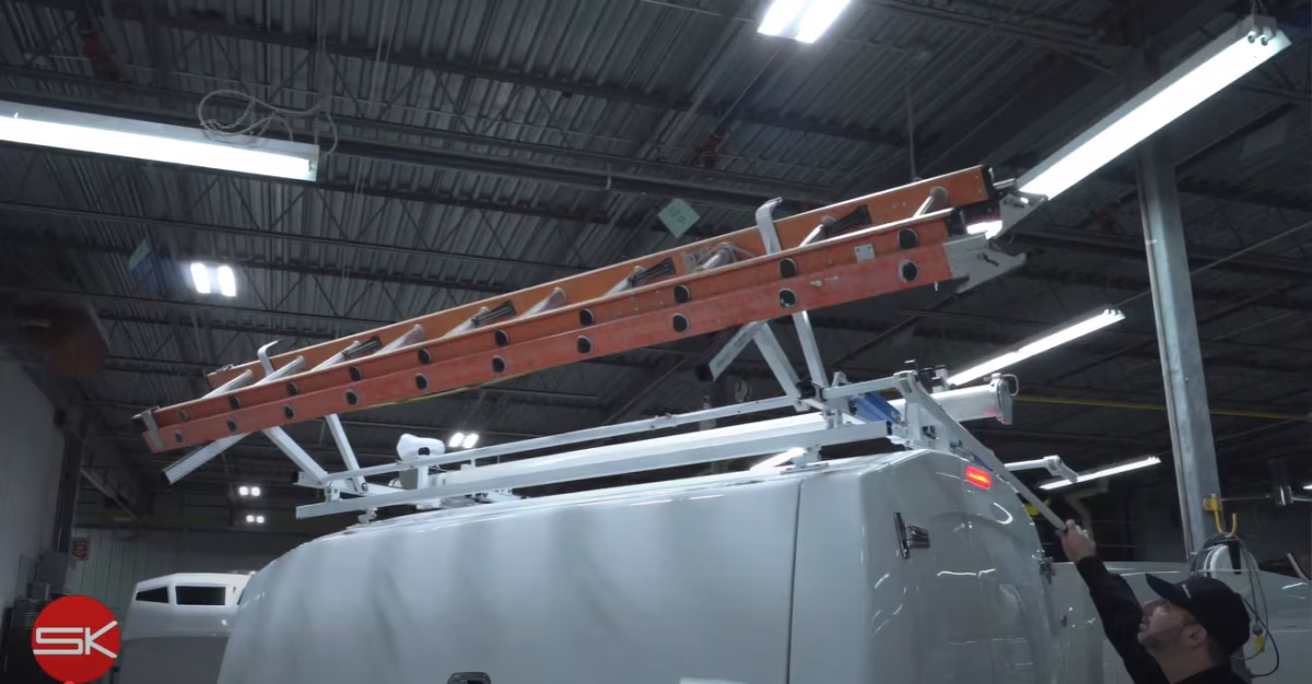 Worker securing an orange extension ladder on top of a white service van inside an industrial workshop