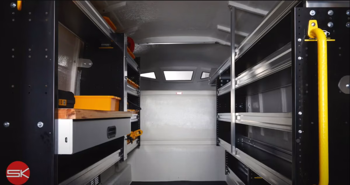 Interior view of a clean and organized utility van with black metal shelving units and a wooden workbench