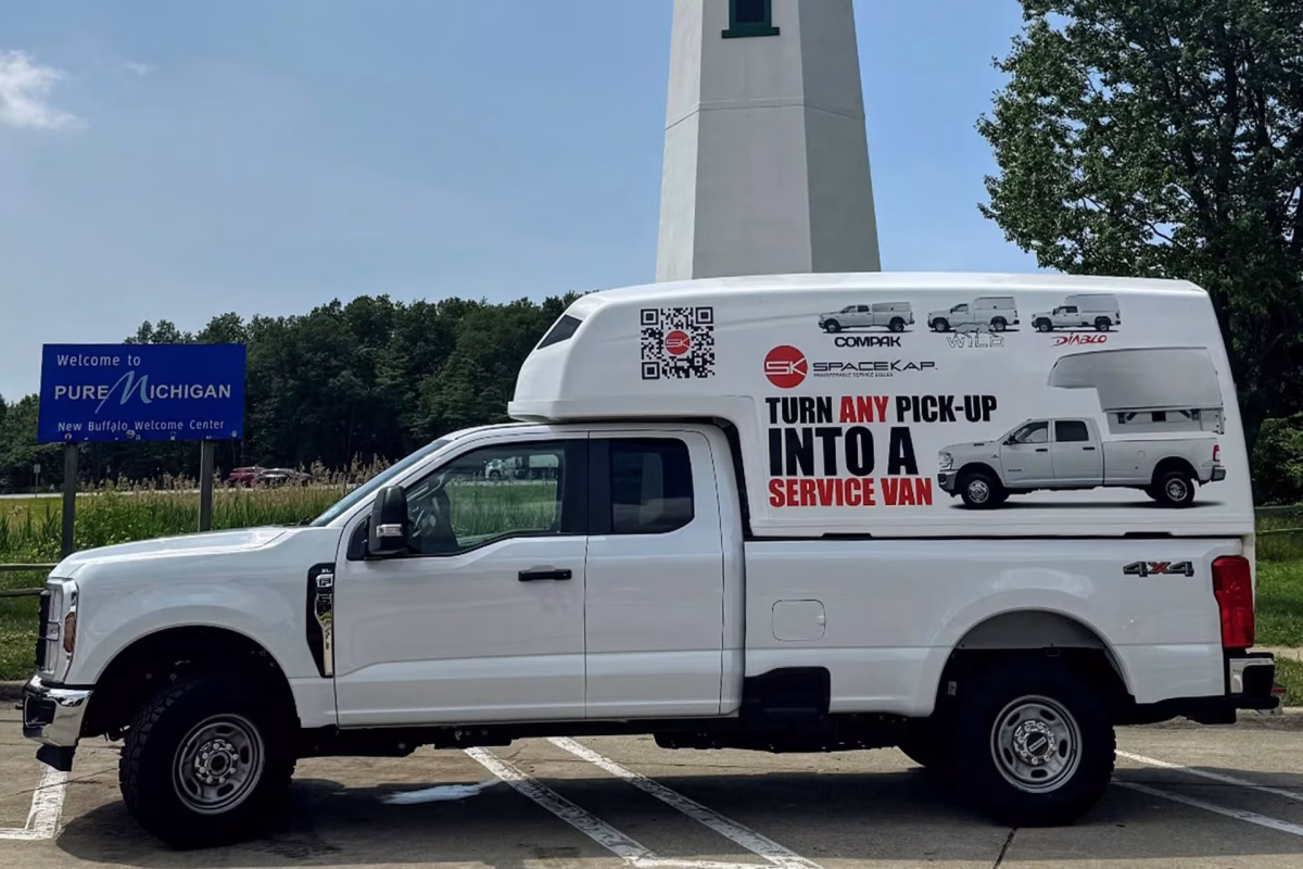 White Ford pickup truck with a large service van SpaceKap parked near a Pure Michigan welcome sign and a white lighthouse.