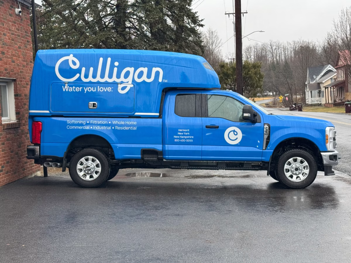 Blue Culligan service truck parked beside a brick building on a wet road, showcasing water softening and filtration services