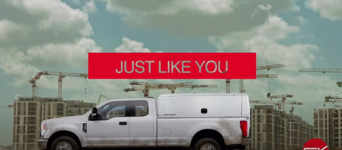 White pickup truck with canopy on construction site background and red banner reading 'JUST LIKE YOU'