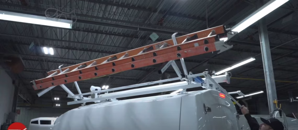 Worker securing an orange extension ladder on top of a white service van inside an industrial workshop